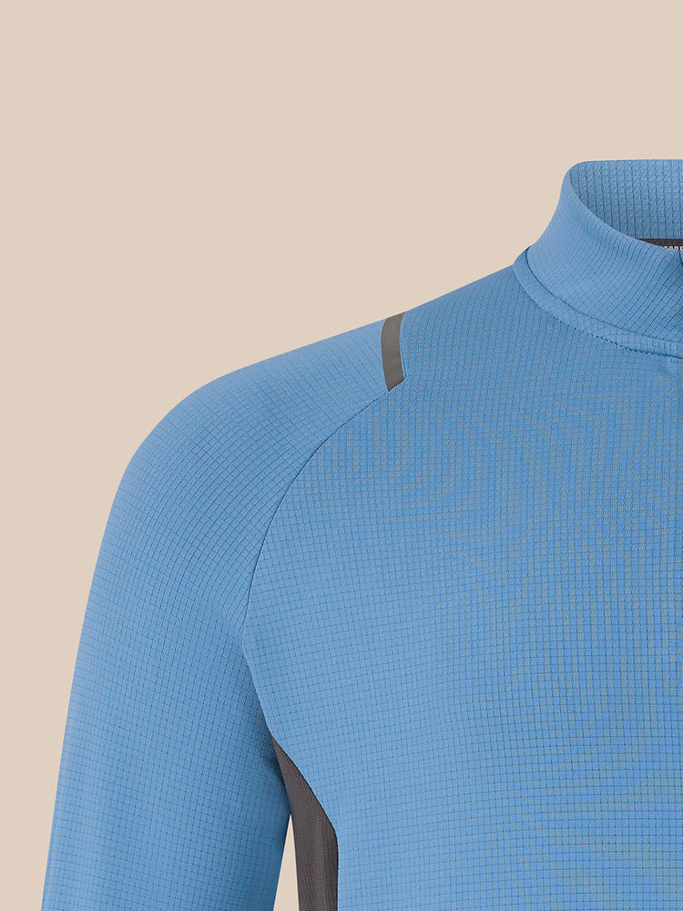 Close-up of a light blue textured athletic top with a mock neck and dark gray shoulder detail, shown against a solid beige background.