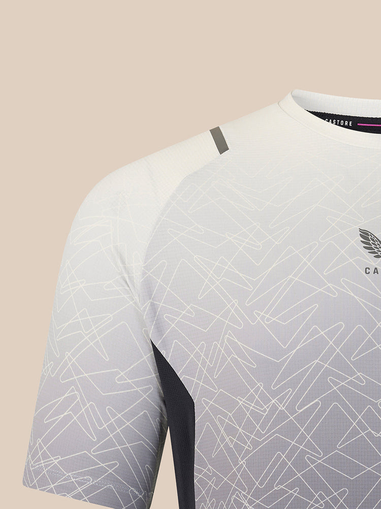 Close-up of a short-sleeve athletic jersey in white and light gray with an allover abstract line pattern, dark side paneling, and a small wing logo on the chest.